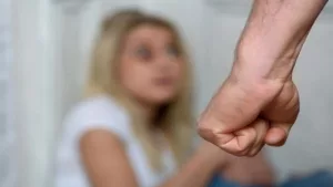 Close-Up of the Fist of a Man Going to Chastise the Girl Sitting on the Floor in the Corner