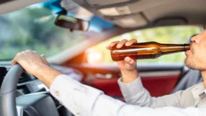 Man Driving While Drinking a Bottle of Beer on a Daylight