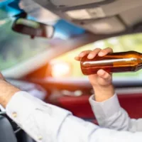 Man Driving While Drinking a Bottle of Beer on a Daylight
